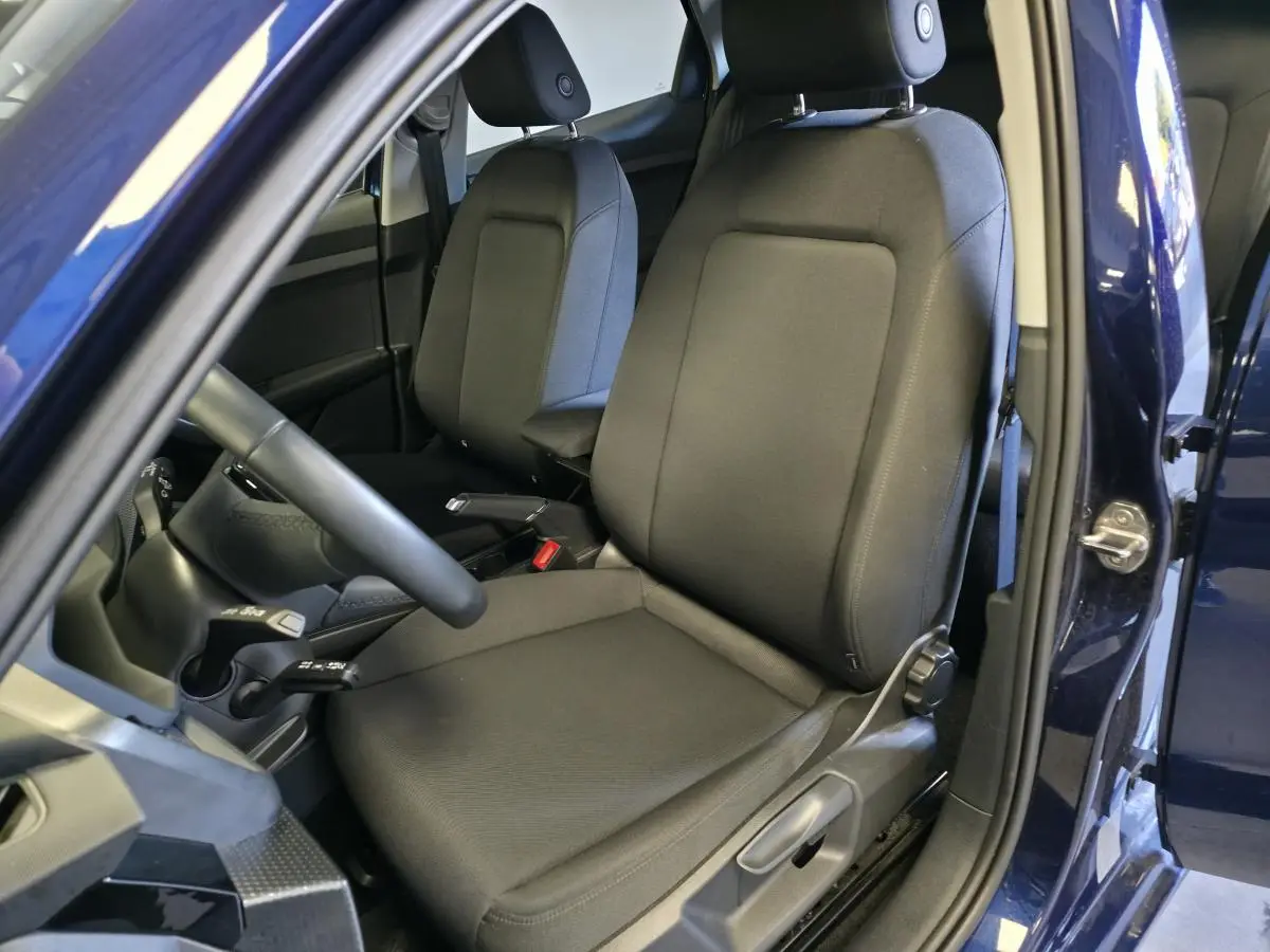 Vue intérieure côté gauche de l'Audi A1 Sportback 2024 bleu, montrant les sièges sport en tissu noir et le volant cuir multifonctions.