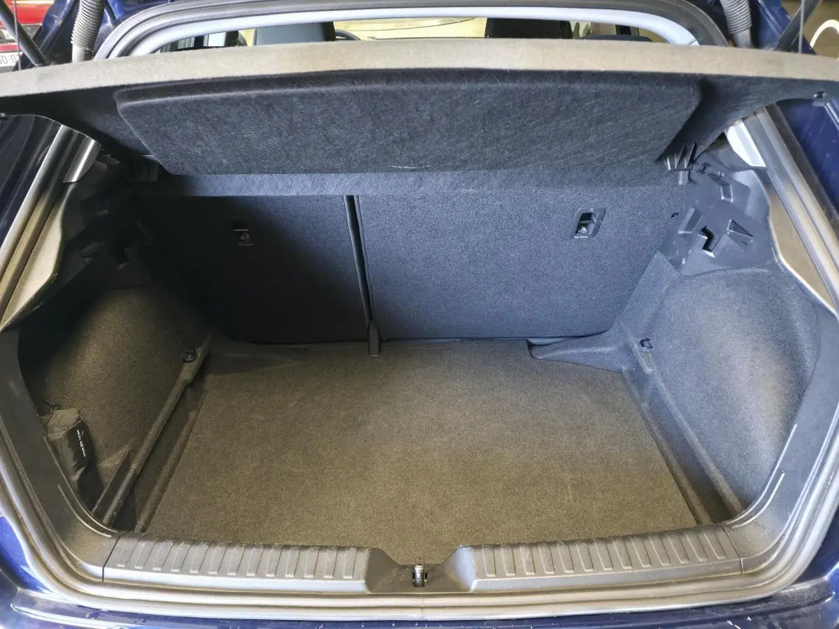 Coffre ouvert d'une Audi A1 Sportback 2024 bleu, montrant l'espace de rangement intérieur et la moquette grise.