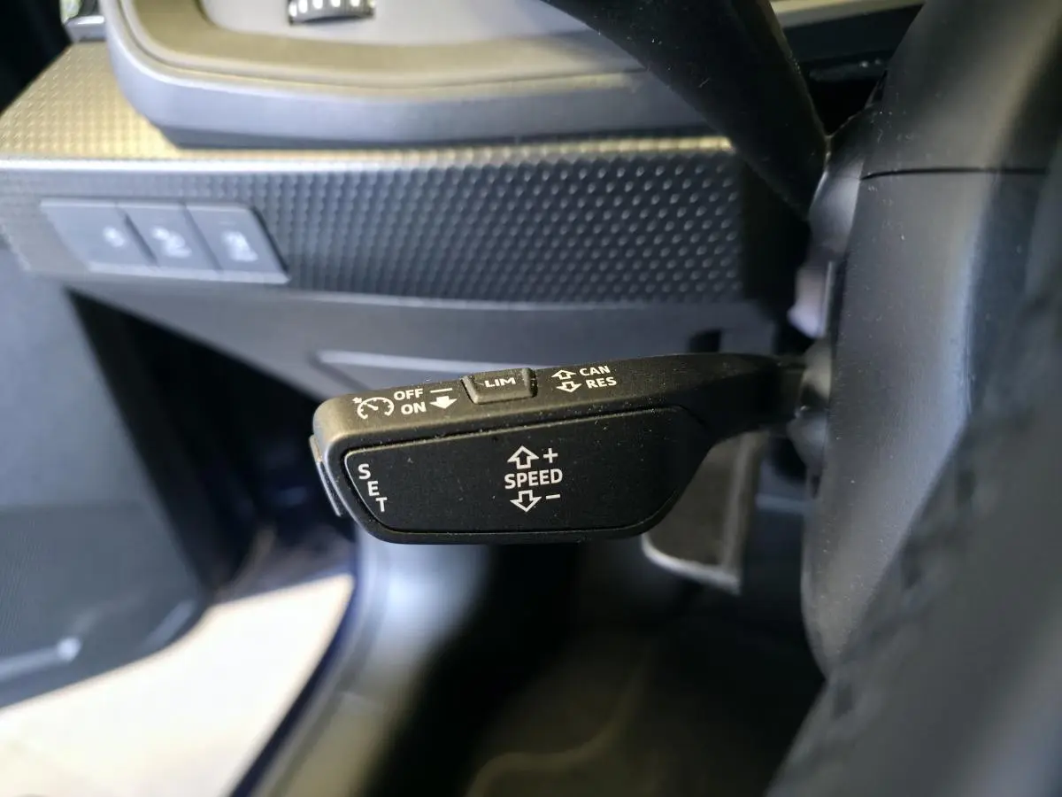 Gros plan sur la commande de régulateur de vitesse à gauche du volant dans l'Audi A1 Sportback bleu 2024.