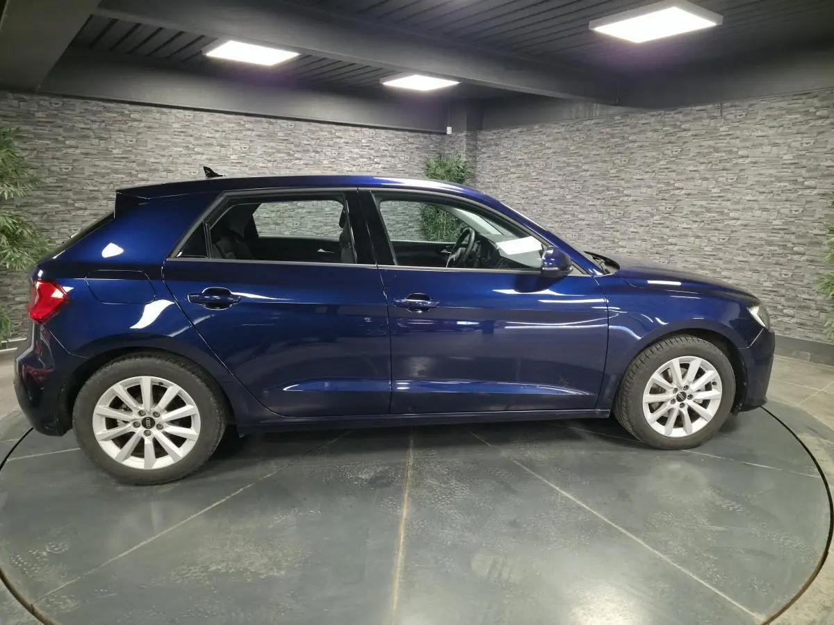 Audi A1 Sportback bleu métallisé vue de profil côté gauche dans un showroom avec mur en pierre grise.