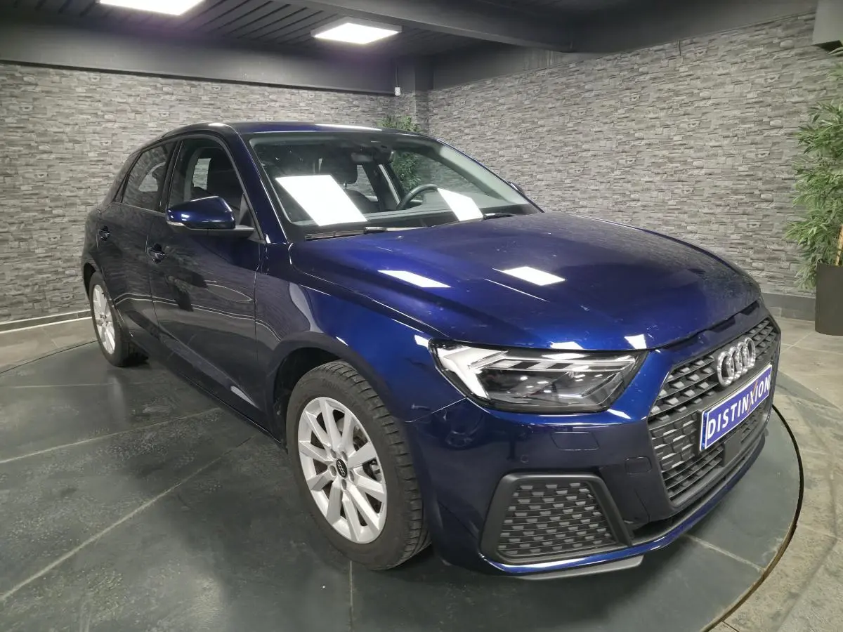 Audi A1 Sportback bleu métallisé vue 3/4 avant droit avec calandre noire et jantes alu 16 pouces dans un showroom.