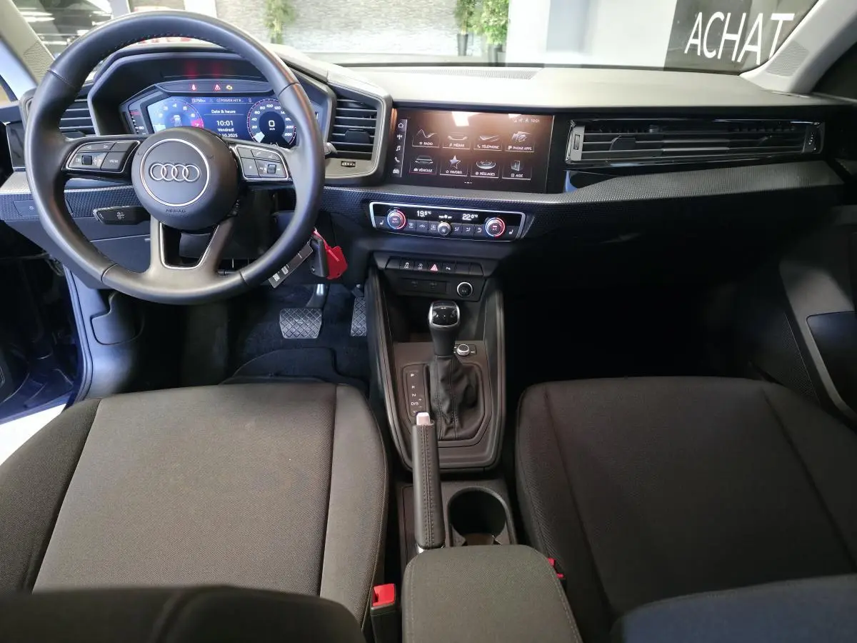 Intérieur de l'Audi A1 Sportback 2024 en vue frontale, tableau de bord noir avec écran digital et volant cuir multifonctions.
