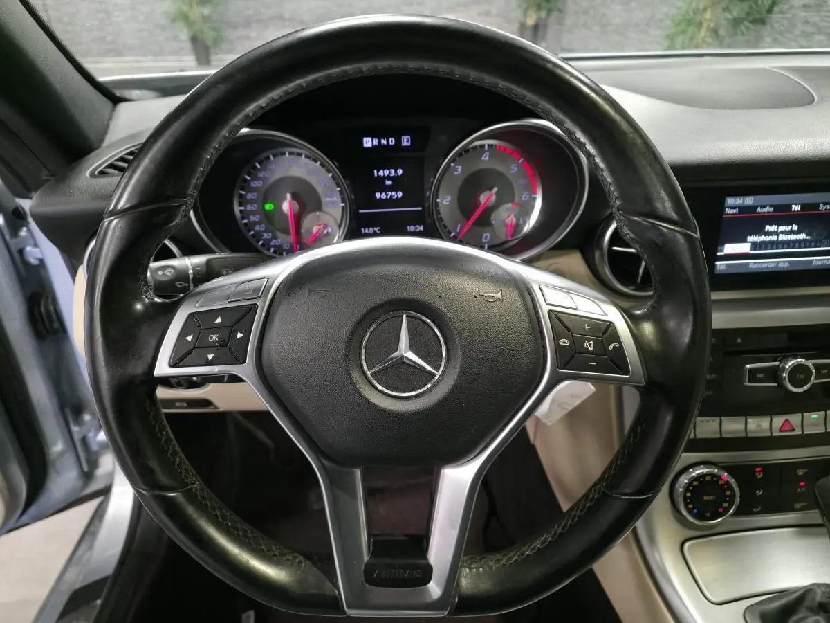 Vue intérieure centrée sur le volant cuir noir de la Mercedes SLK 250 CDI avec tableau de bord et écran multimédia visibles.