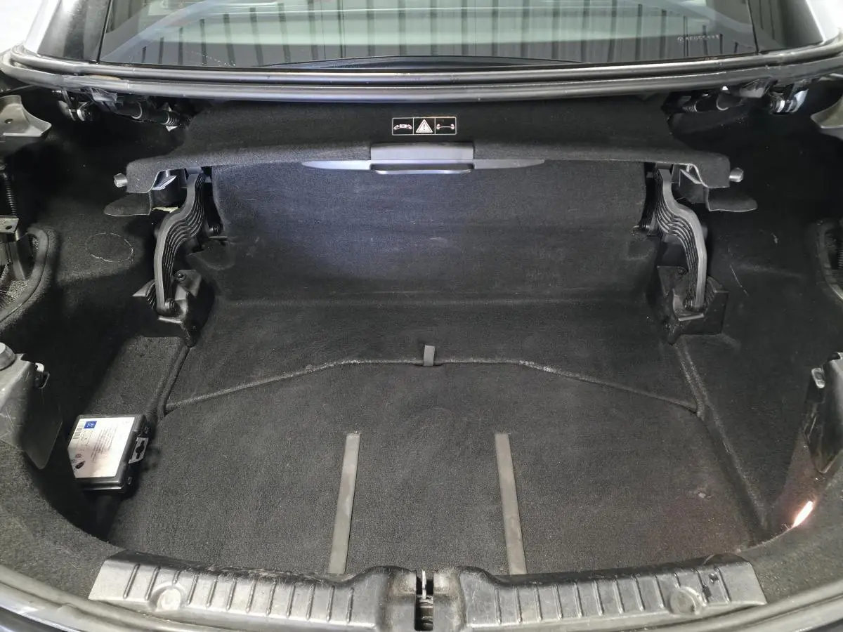 Coffre ouvert d'une Mercedes SLK 250 CDI gris, montrant l'espace de rangement avec moquette noire et charnières visibles.