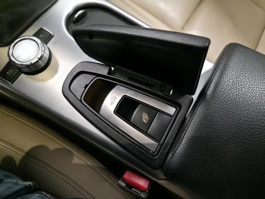 Détail de la console centrale avec accoudoir cuir noir et commandes d'ouverture de coffre et capote sur Mercedes SLK gris.