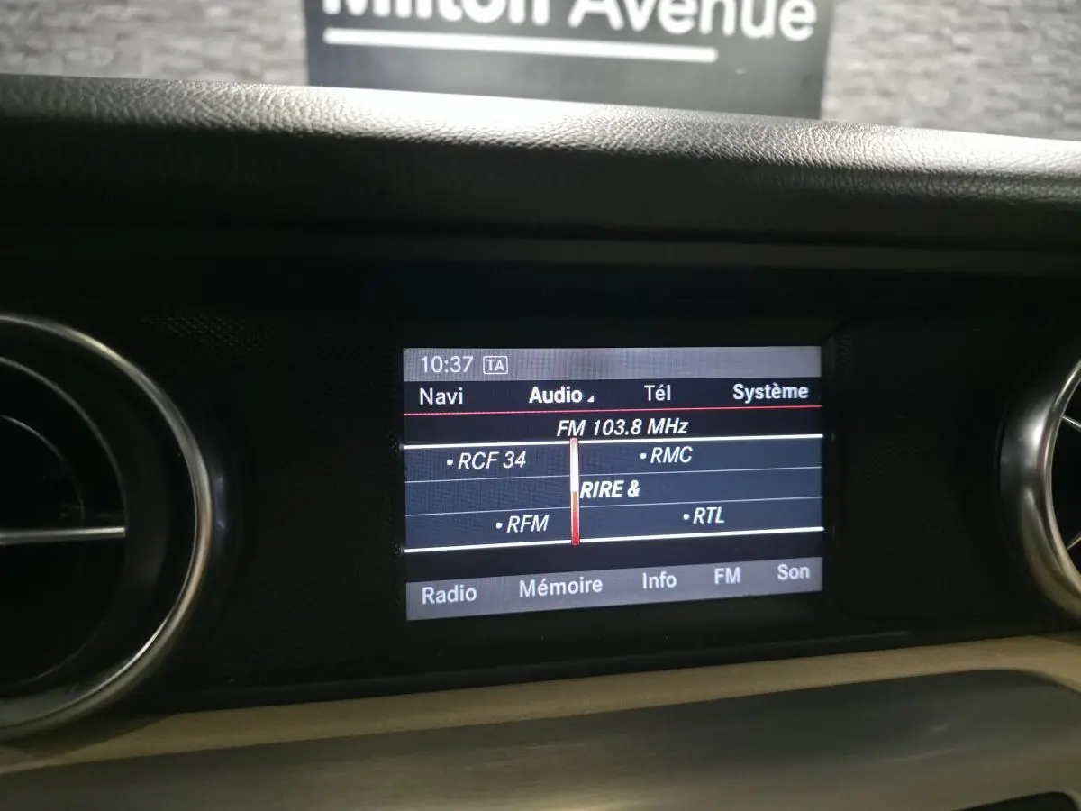 Écran central de navigation et audio affichant la fréquence FM 103.8 MHz dans l'habitacle d'une Mercedes SLK 250 CDI gris