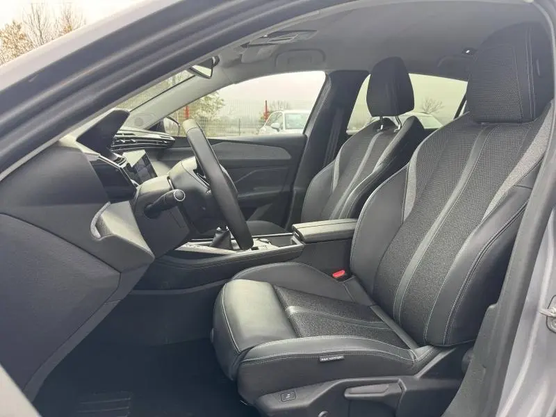 Vue intérieure côté conducteur du Peugeot 308 2024 gris Artense, avec sièges en cuir et tissu, volant et console centrale visibles.
