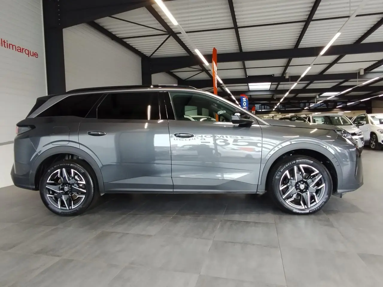 Peugeot 5008 gris titanium vue de profil côté droit en intérieur avec jantes alliage 19 pouces diamantées.