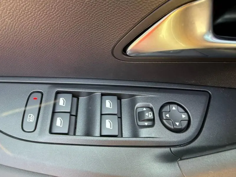 Gros plan sur les commandes des vitres et rétroviseurs côté conducteur d’une Peugeot 2008 rouge Elixir, intérieur noir.