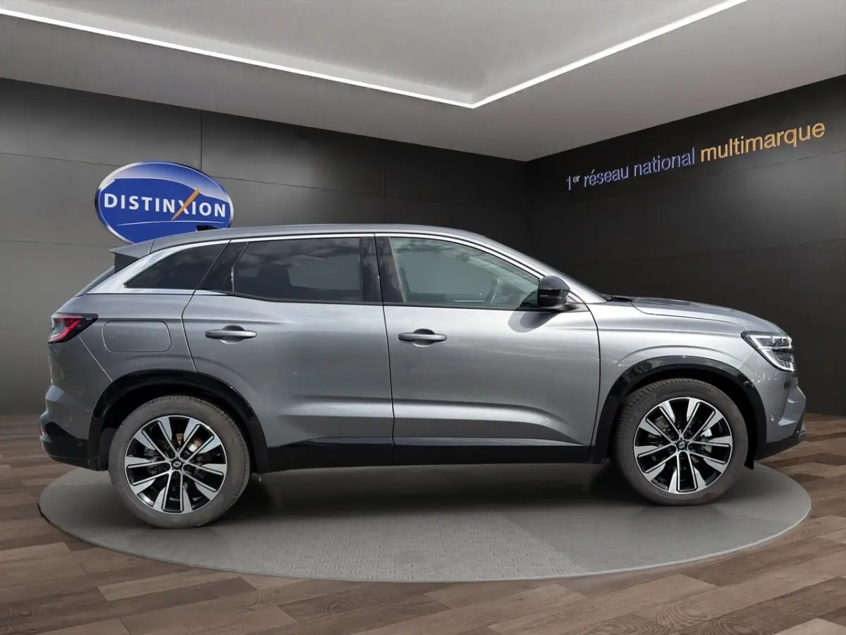 Profil droit d’un Renault Austral gris foncé avec jantes alliage bicolores, présenté en showroom intérieur.