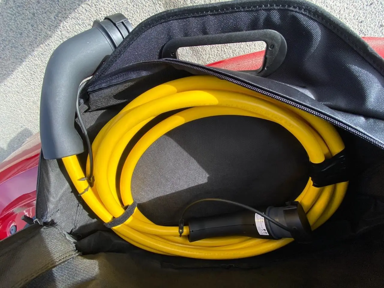 Câble de recharge jaune enroulé dans un sac noir posé sur le coffre rouge d'une Fiat 500 Cabriolet Electrique.