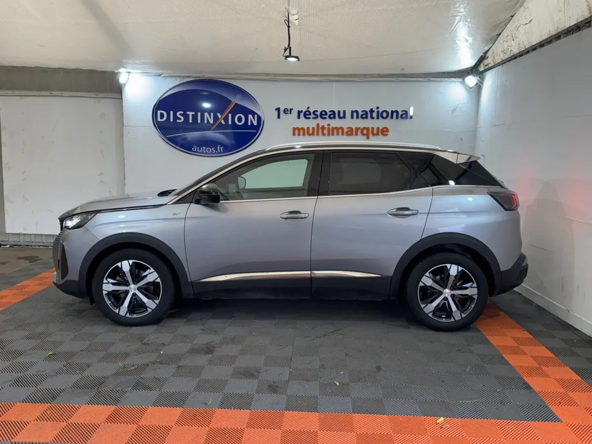 Vue de profil côté gauche d’un Peugeot 3008 GT gris clair stationné en intérieur avec jantes bicolores et toit noir.