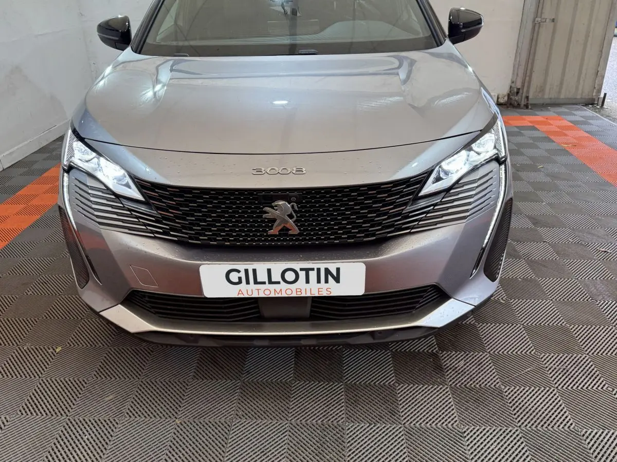Vue avant d’un Peugeot 3008 gris clair avec calandre noire et phares LED allumés dans un garage.