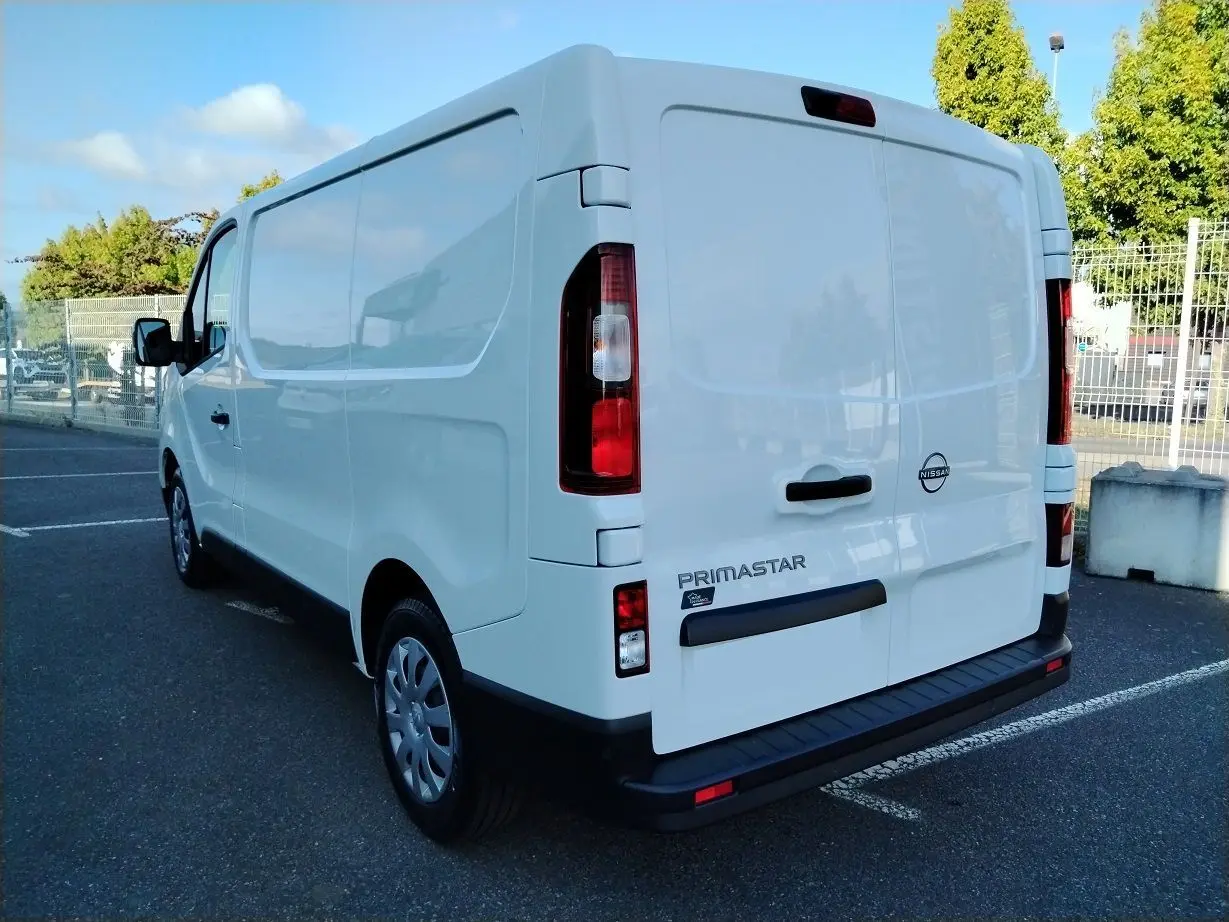 Vue 3/4 arrière droite d'un utilitaire Nissan Primastar blanc avec logo et marquage visible sur porte arrière.