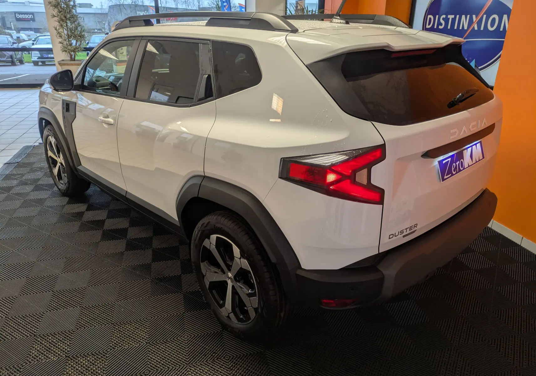 Vue 3/4 arrière droite d'un Dacia Duster blanc glacier 2025 en hybride, avec jantes alliage 18 pouces et feux arrière allumés.