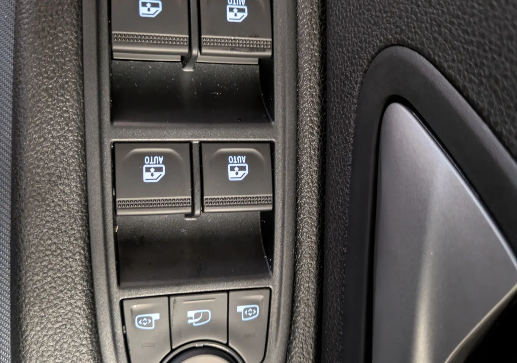 Gros plan sur les commandes de lève-vitres et réglage des rétroviseurs côté conducteur d'un Dacia Duster blanc glacier 2025.