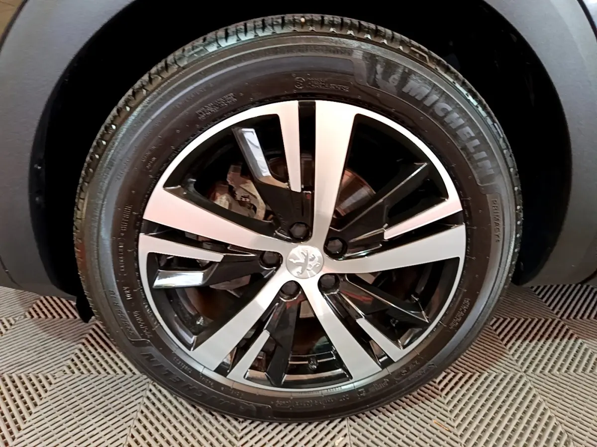 Gros plan sur la roue avant droite du Peugeot 3008 noir, mettant en valeur la jante alliage bicolore au design moderne.