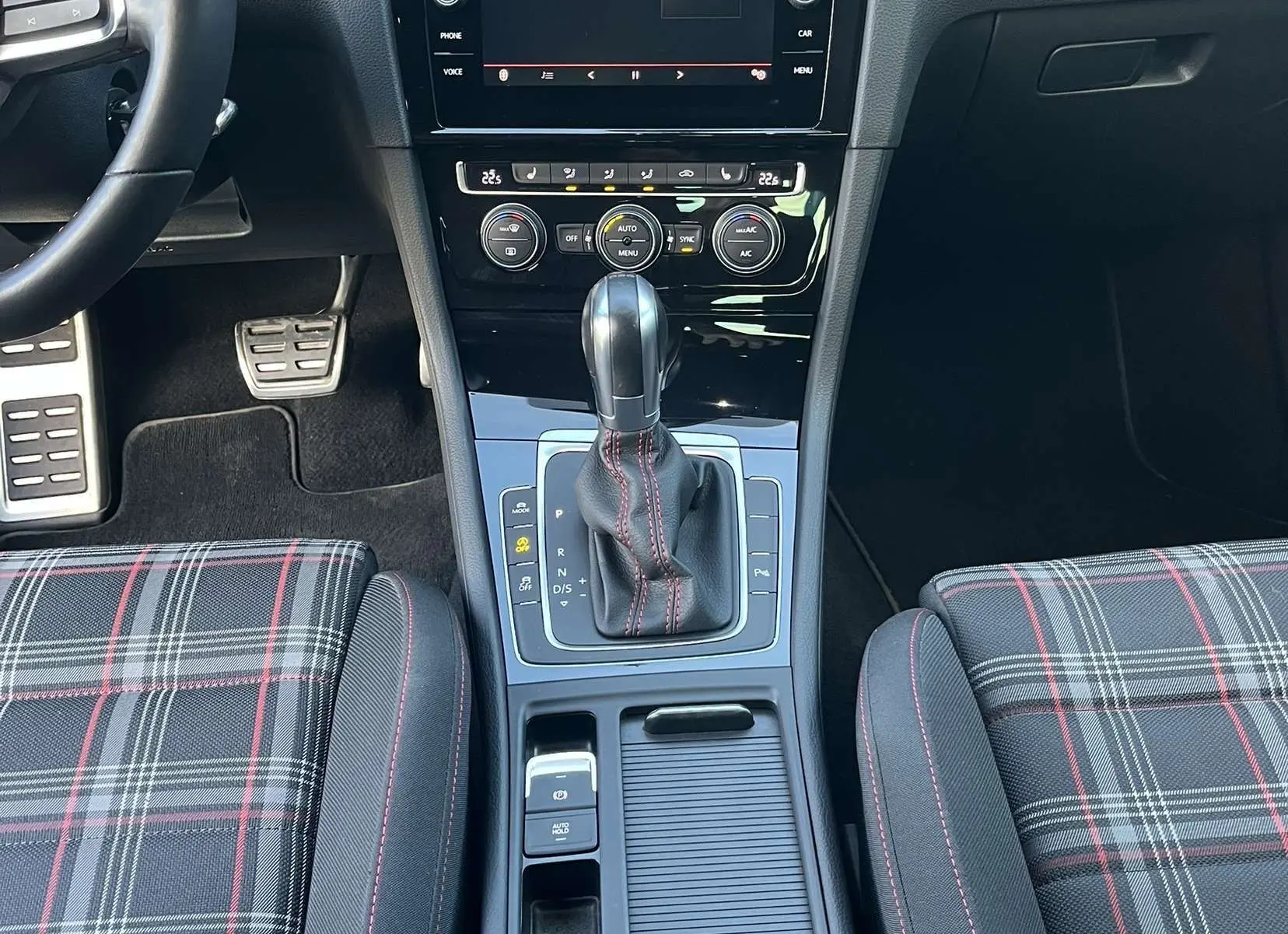 Vue intérieure centrée sur la console centrale et la boîte automatique d'une Volkswagen Golf GTI Performance avec sièges à motif tartan.