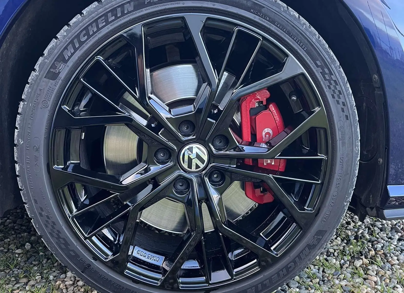 Gros plan sur la roue avant droite d'une Volkswagen Golf GTI Performance bleu lapiz, jante noire et étrier de frein rouge visible.