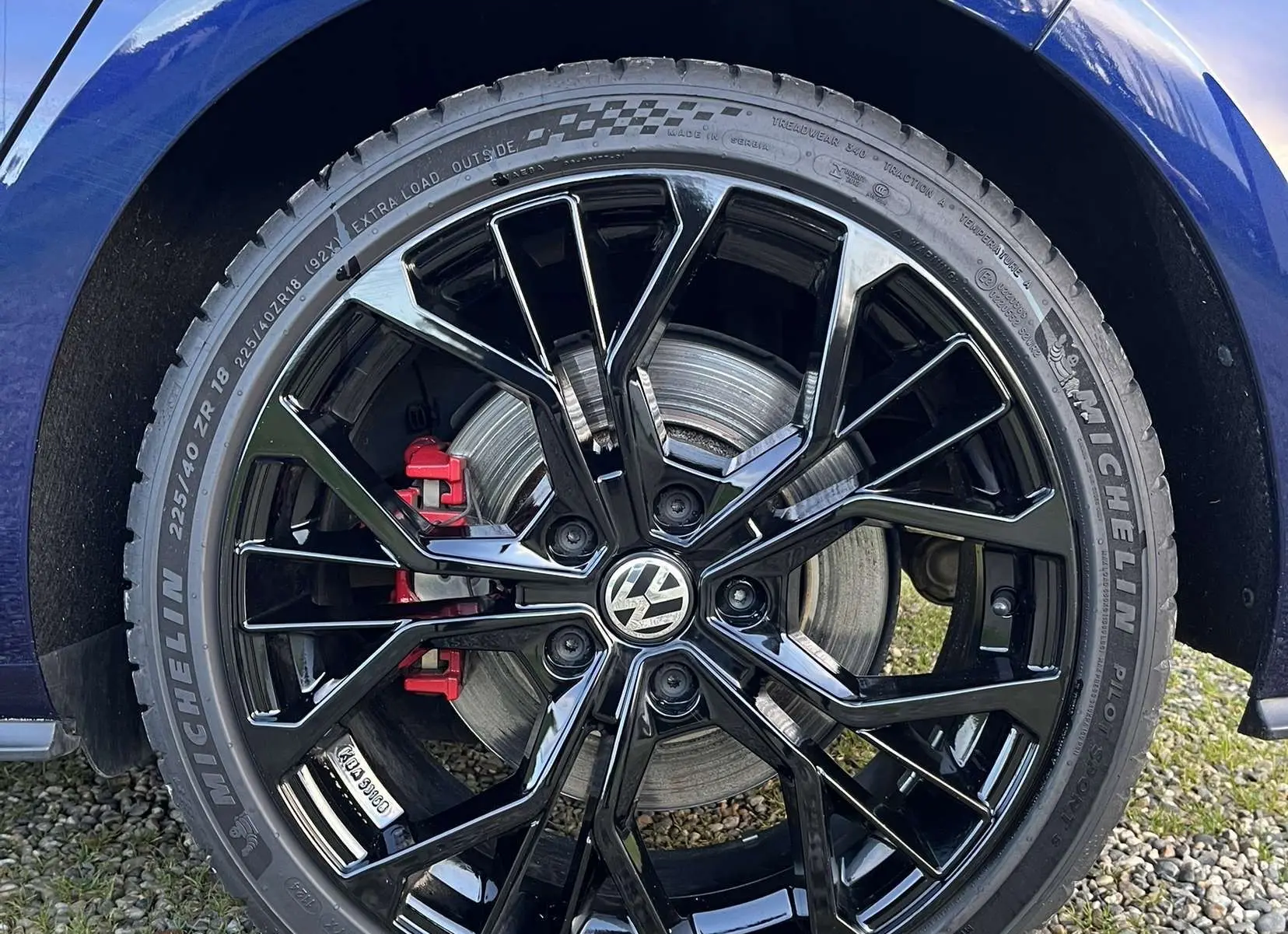 Gros plan sur la roue arrière droite d'une Volkswagen Golf VII bleu lapiz avec jante noire brillante et étrier de frein rouge.