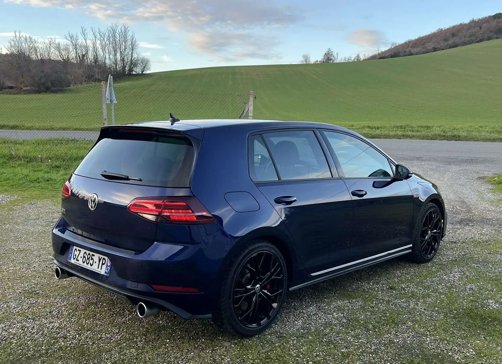 Volkswagen Golf VII GTI Performance bleu Lapis Metal vue 3/4 arrière droit avec jantes noires et double sortie d’échappement.