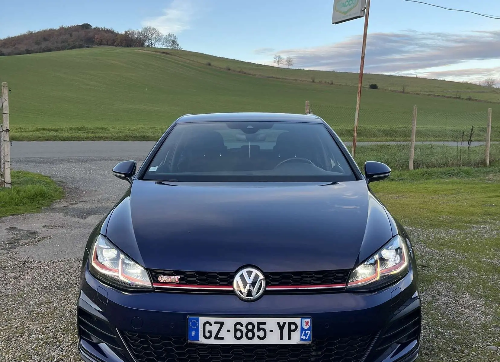 Vue de face d'une Volkswagen Golf VII GTI Performance bleu lapiz metal avec calandre noire et bande rouge distinctive.