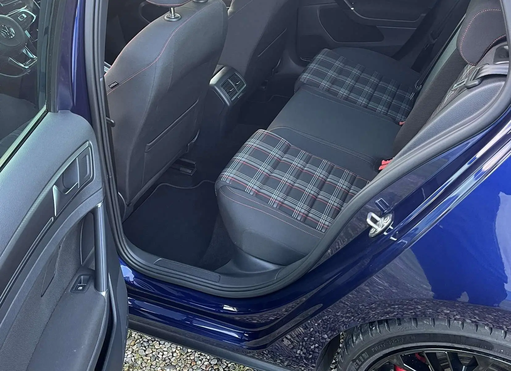 Vue intérieure arrière côté gauche d'une Volkswagen Golf VII GTI Performance bleu lapiz, sièges arrière à motif tartan et jantes noires visibles.