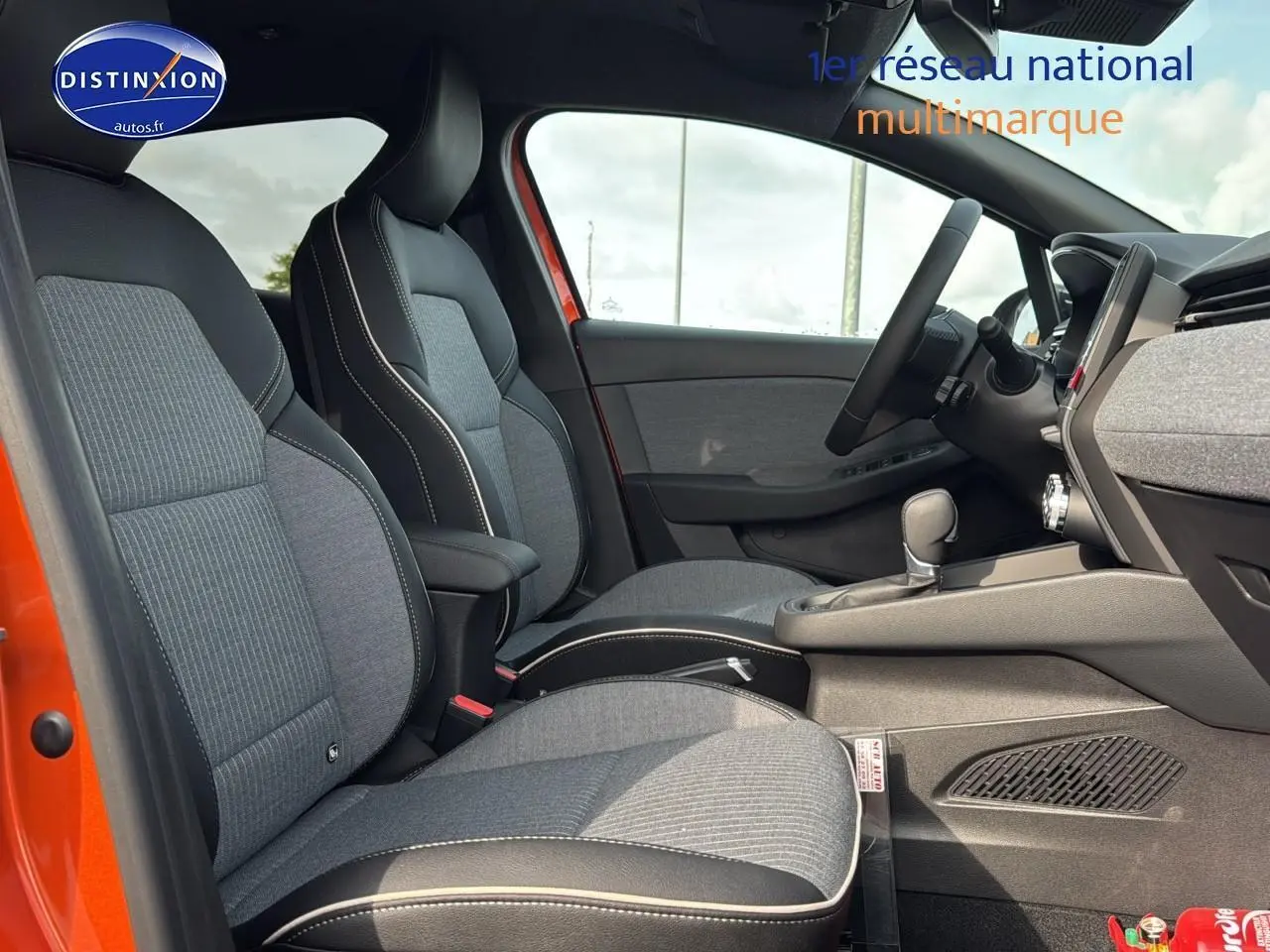 Intérieur avant de la Renault Clio V orange Valencia, sièges sport gris avec surpiqûres blanches et accoudoir central.