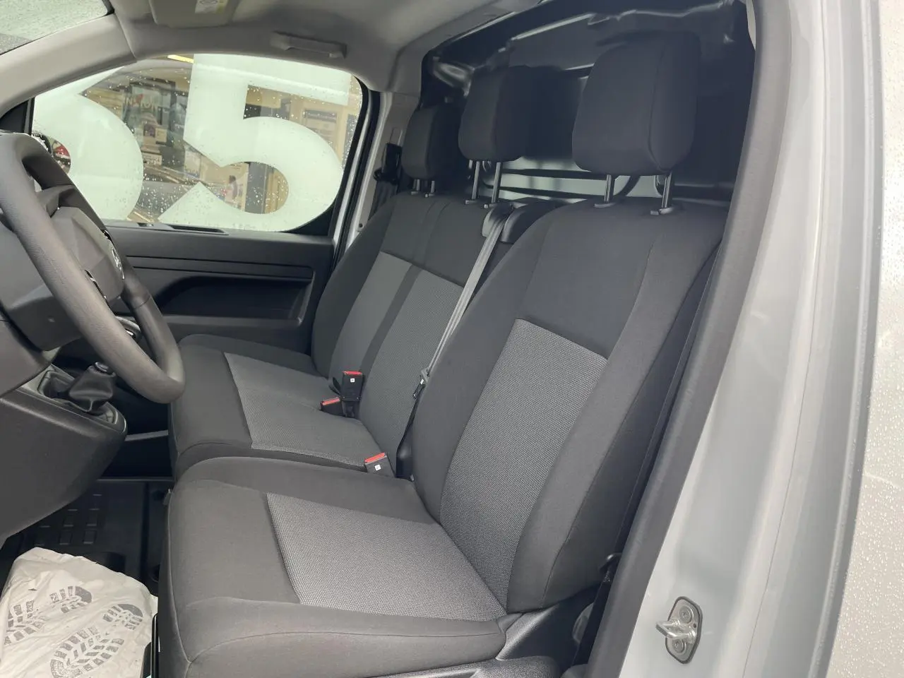 Intérieur côté conducteur d'un Opel Vivaro blanc 2024, montrant la banquette 3 places en tissu bi-ton noir et gris.