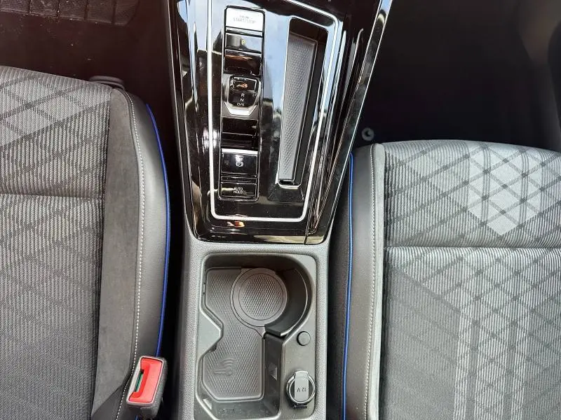 Vue plongeante sur la console centrale noire brillante et les sièges gris à surpiqûres bleues de la Volkswagen Golf R-Line 2025.