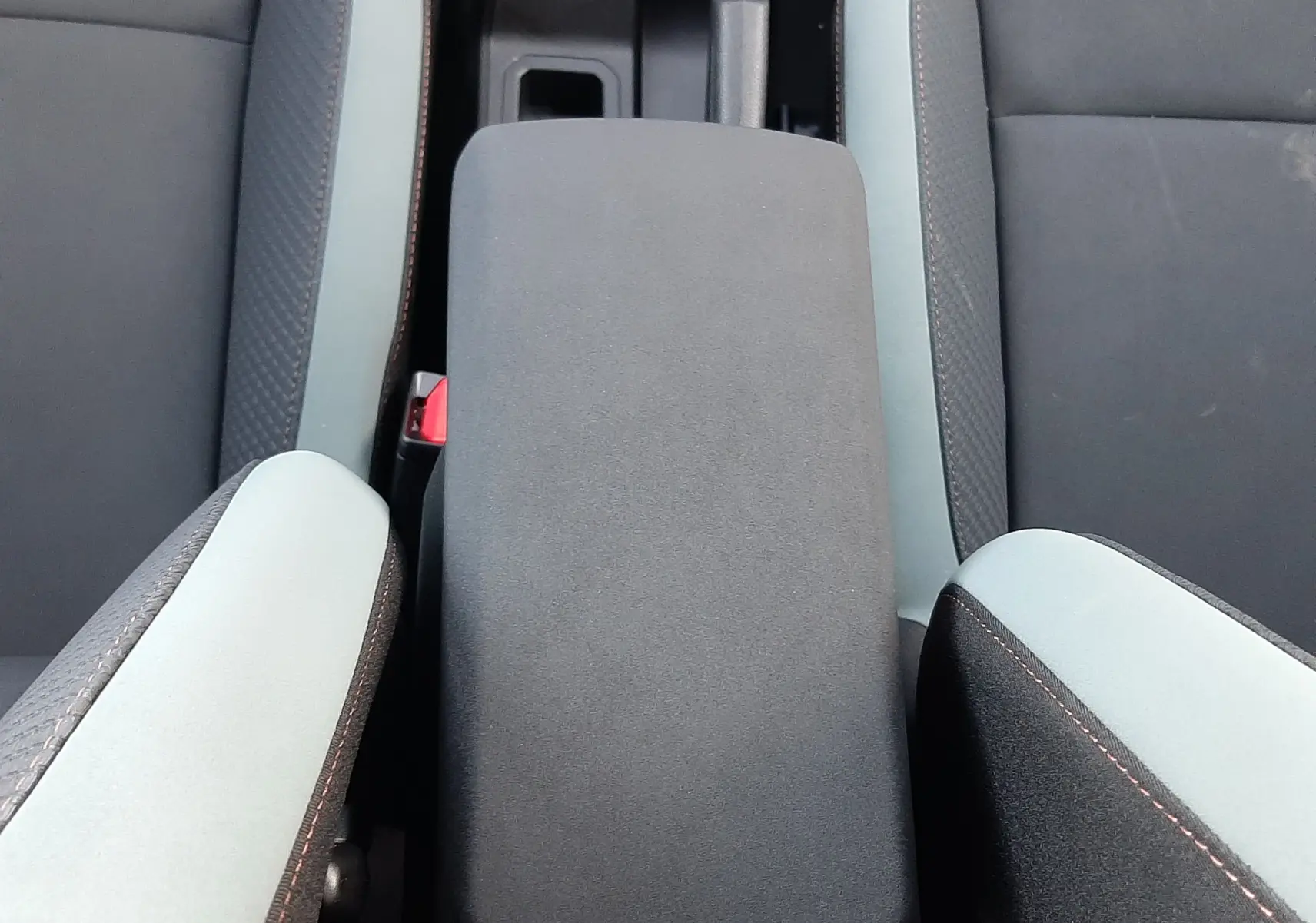 Vue plongeante sur l'accoudoir central et sièges tissu gris clair et foncé du Dacia Duster 1.6 Hybrid 2025 Sandstone.