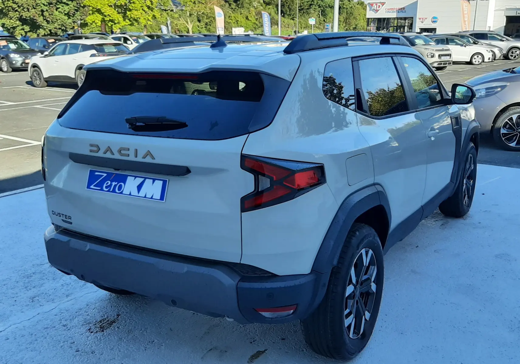 Vue 3/4 arrière droite du Dacia Duster 2025 hybride couleur Sandstone avec barres de toit et jantes biton.