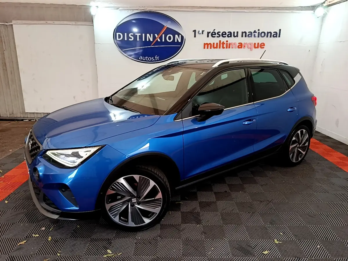 SEAT Arona bleu en 3/4 avant droit, toit noir et jantes alliage distinctives dans un showroom intérieur.
