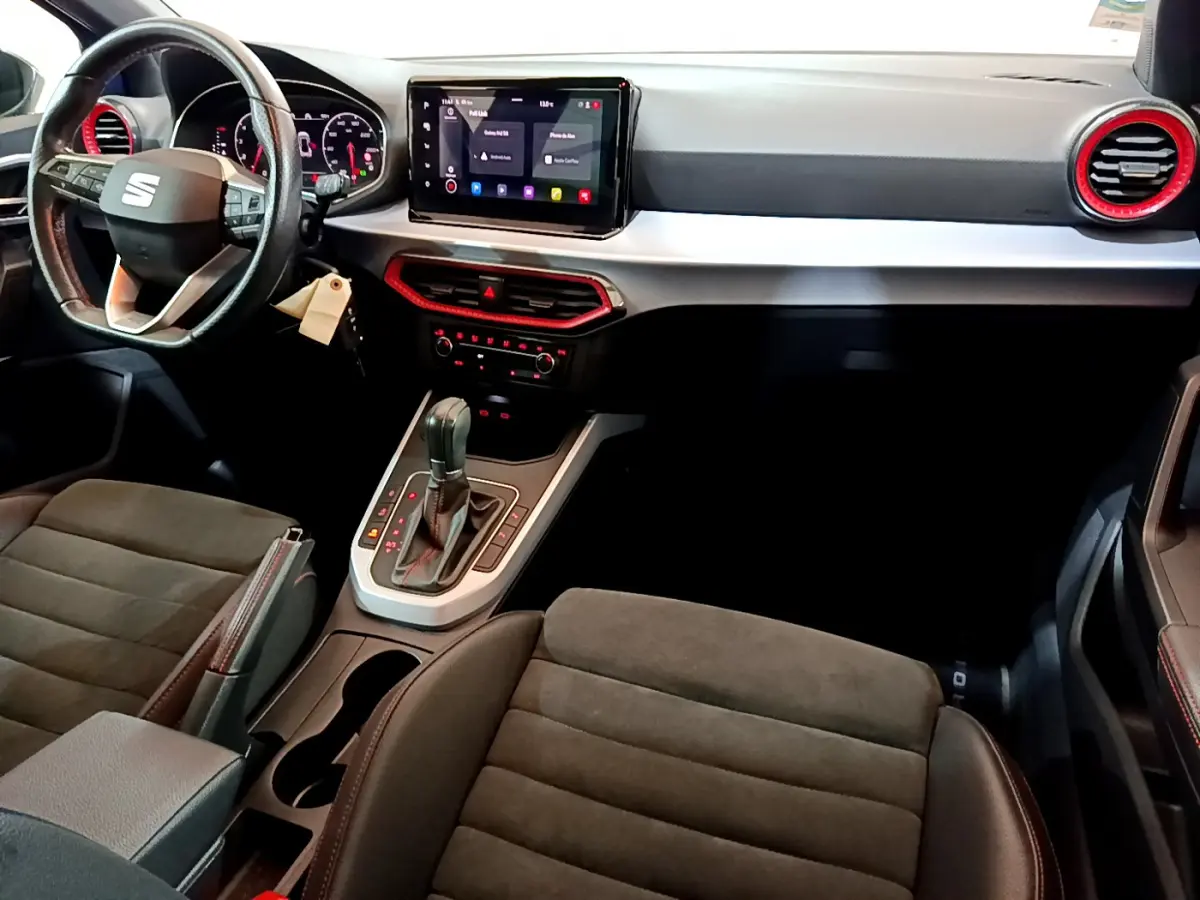 Intérieur du SEAT Arona 2022 vu côté conducteur, tableau de bord noir avec touches rouges et écran tactile central.