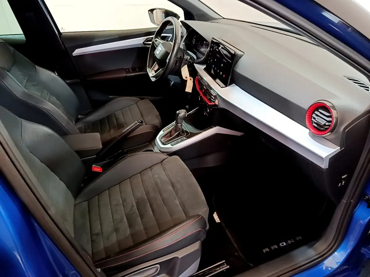 Intérieur côté conducteur d'une SEAT Arona bleu 2022, avec tableau de bord moderne et sièges noirs à surpiqûres rouges.