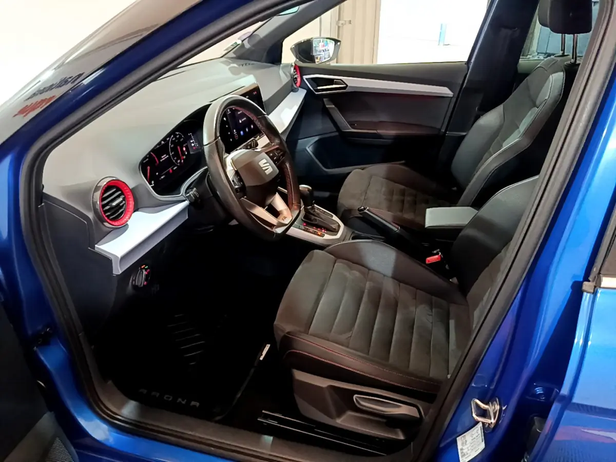 Intérieur côté conducteur d'une SEAT Arona bleu 2022, montrant sièges noirs et tableau de bord moderne avec volant cuir.