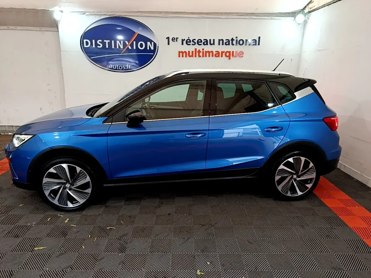 Profil côté gauche d'un SEAT Arona bleu 2022 avec toit noir et jantes alliage stylisées en intérieur showroom.