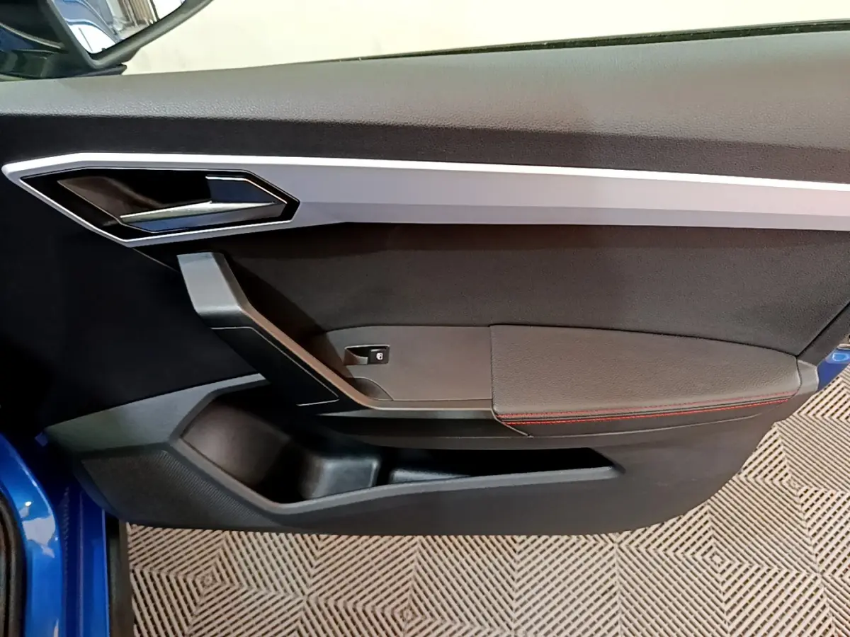 Porte intérieure côté gauche de la SEAT Arona bleu 2022 avec surpiqûres rouges et poignée argentée.