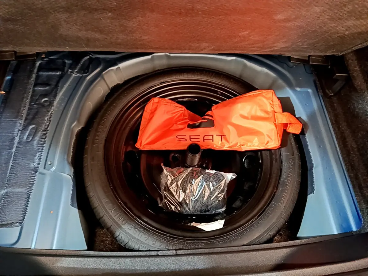 Vue plongeante sur la roue de secours noire dans le coffre bleu du SEAT Arona avec un sac orange marqué SEAT.