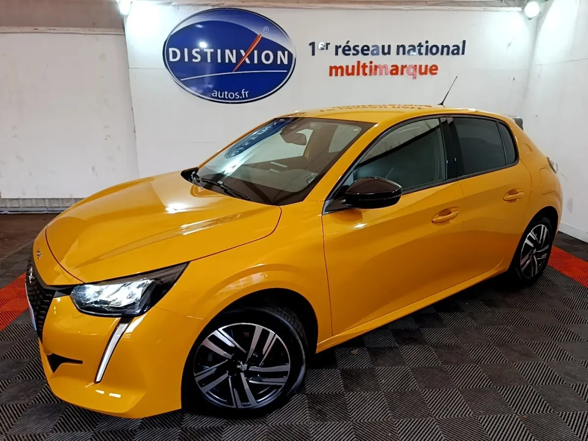 Peugeot 208 jaune vue 3/4 avant droit, feux LED distinctifs et jantes alliage noires en intérieur showroom.