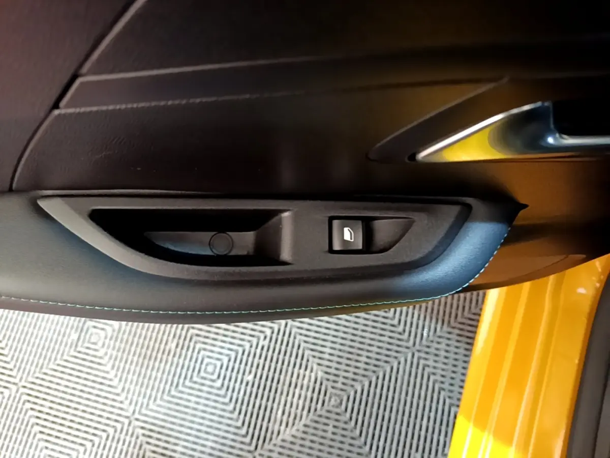 Poignée intérieure côté gauche de porte PEUGEOT 208 jaune 2023 avec bouton de verrouillage et surpiqûres bleues.