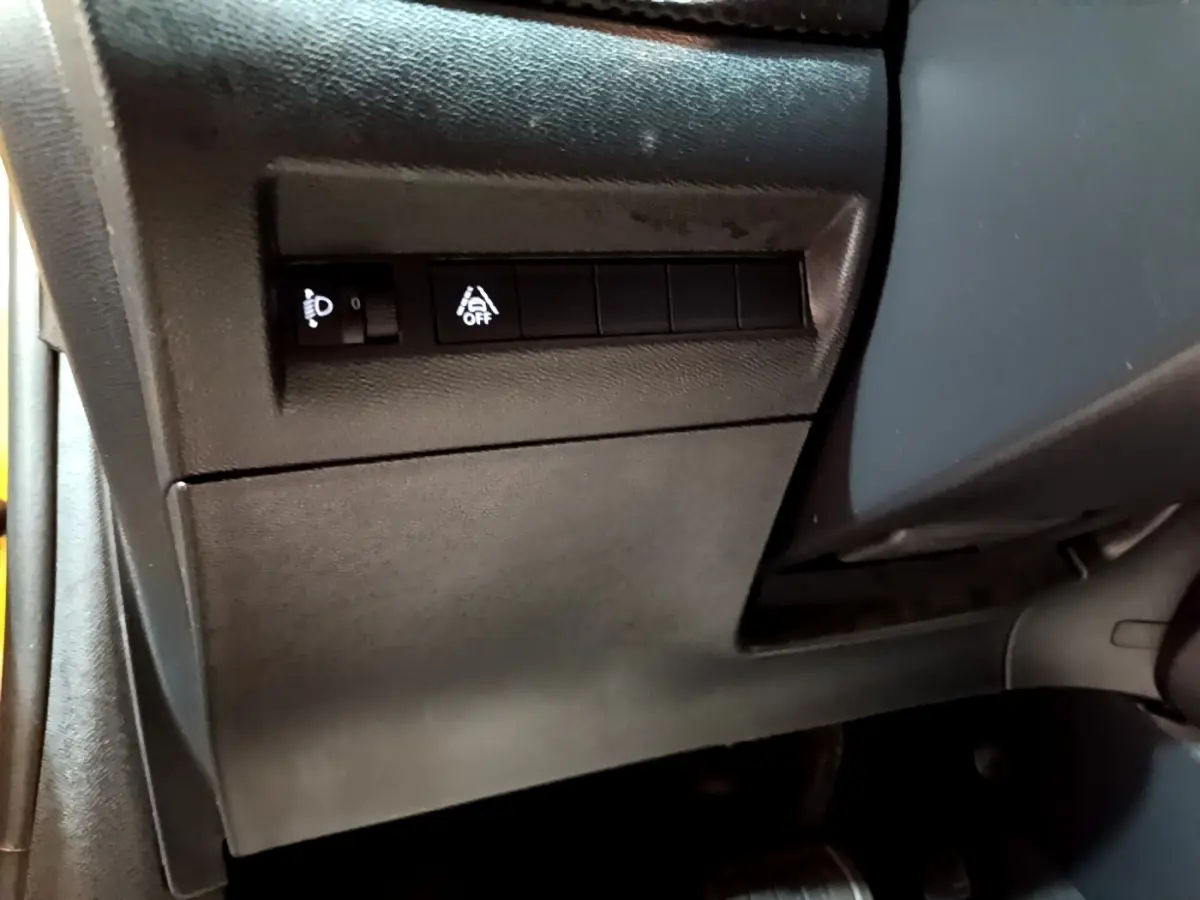Détail intérieur côté gauche de la Peugeot 208 jaune 2023, avec commandes d'éclairage et d'aide à la conduite.