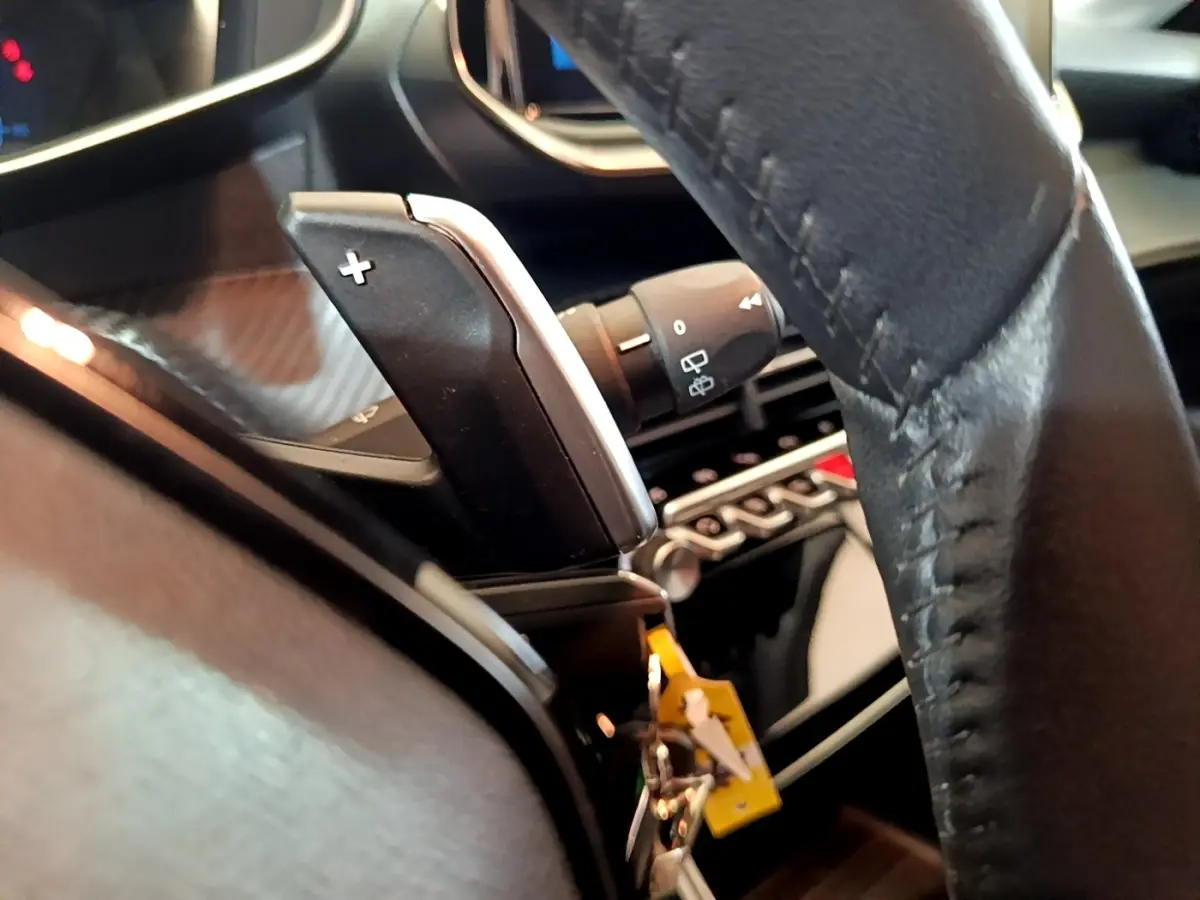 Gros plan sur la palette de changement de vitesse droite et volant cuir noir de la Peugeot 208 jaune 2023.