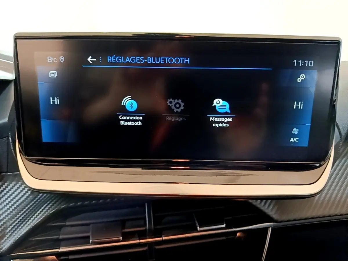 Écran tactile central de la Peugeot 208 jaune 2023 affichant les réglages Bluetooth, vue intérieure frontale.