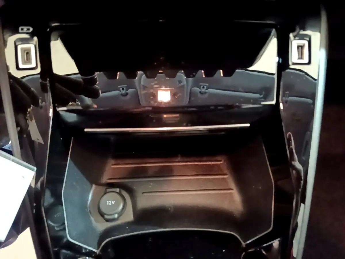 Gros plan sur la console centrale noire de la Peugeot 208, avec prise 12V visible au centre.