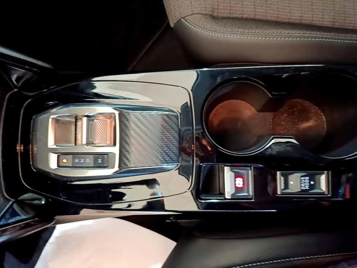 Vue plongeante sur la console centrale noire brillante de la Peugeot 208 jaune, avec la commande de boîte automatique et porte-gobelets.