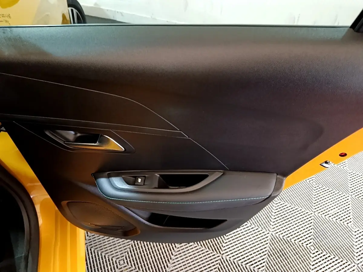 Vue rapprochée de la porte intérieure côté gauche d'une Peugeot 208 jaune avec garniture noire et surpiqûres bleues.
