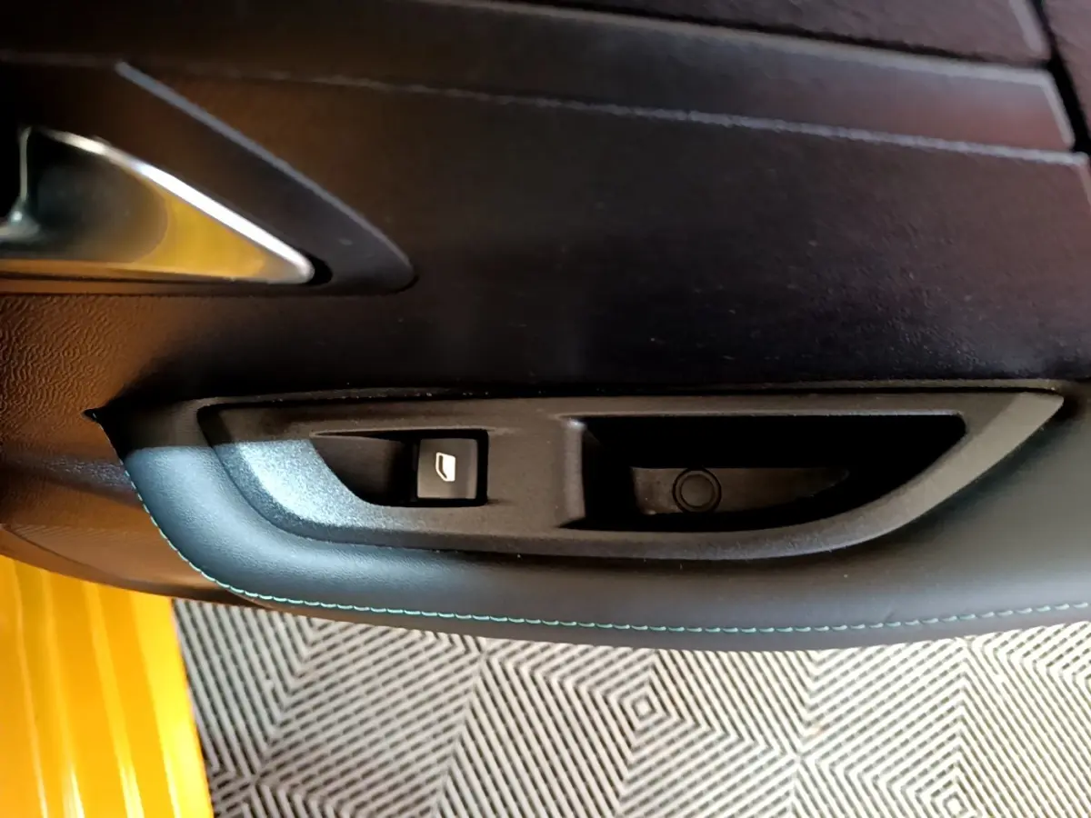 Détail de la commande de lève-vitre sur la porte intérieure d'une Peugeot 208 jaune, finition Allure Pack.