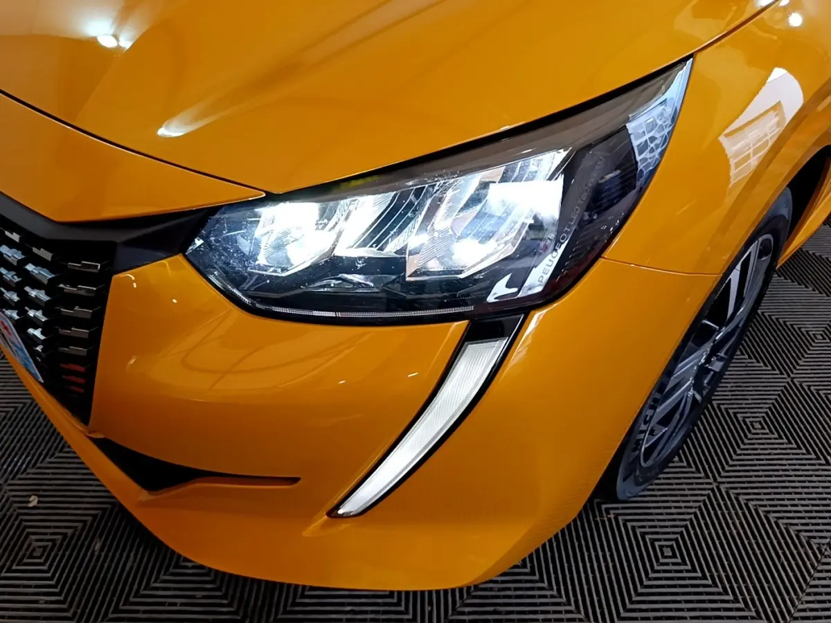 Gros plan sur l'avant droit jaune vif de la Peugeot 208 2023, mettant en valeur son phare LED et la jante alliage.