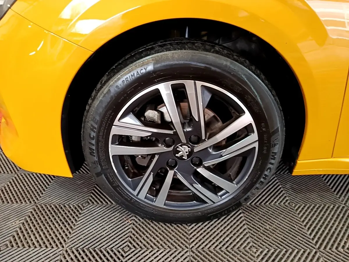 Gros plan sur la roue avant gauche d’une Peugeot 208 jaune 2023 avec jante alliage et logo lion au centre.